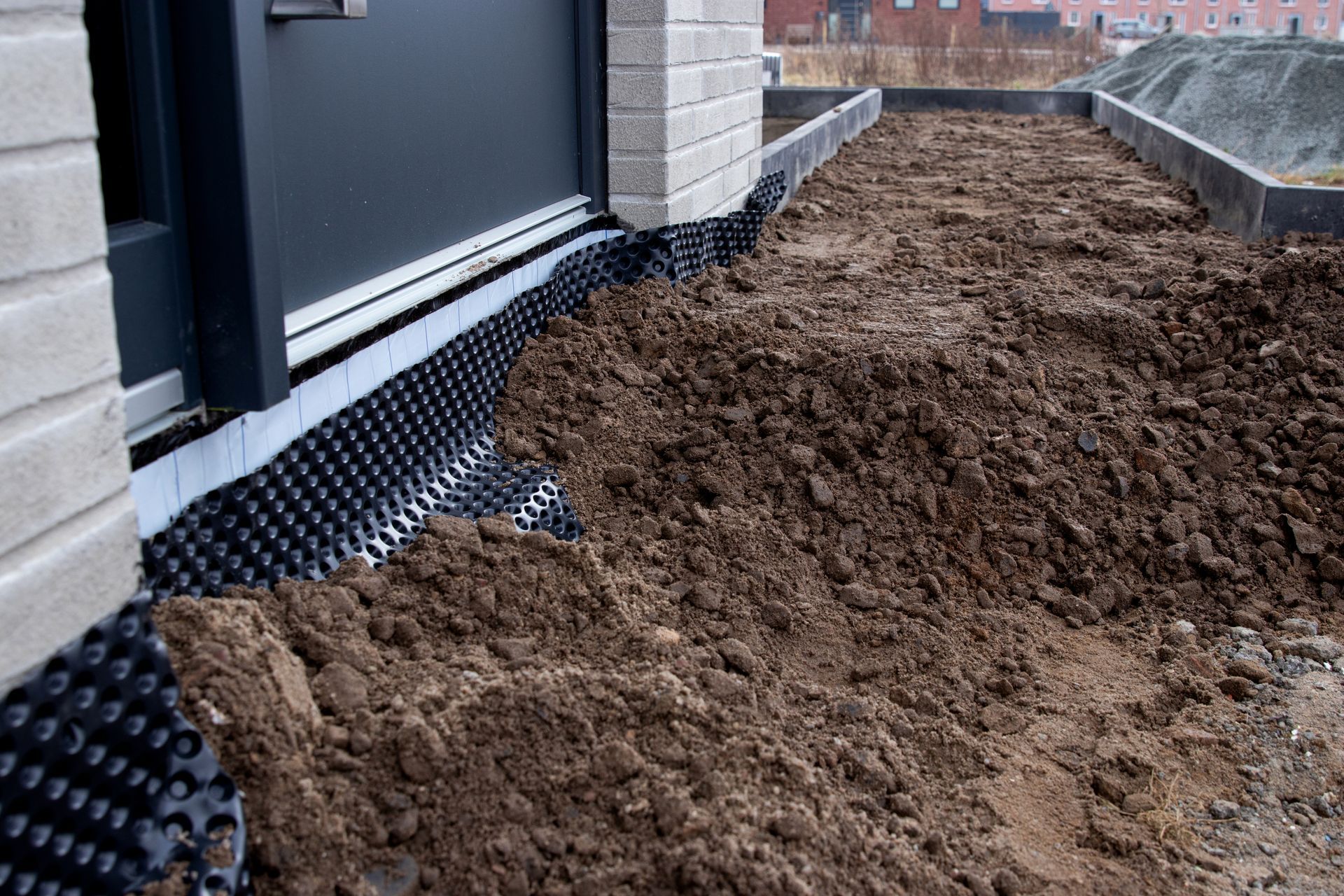 Fondations de maison avec membrane de drainage noire et terre empilée le long du mur extérieur