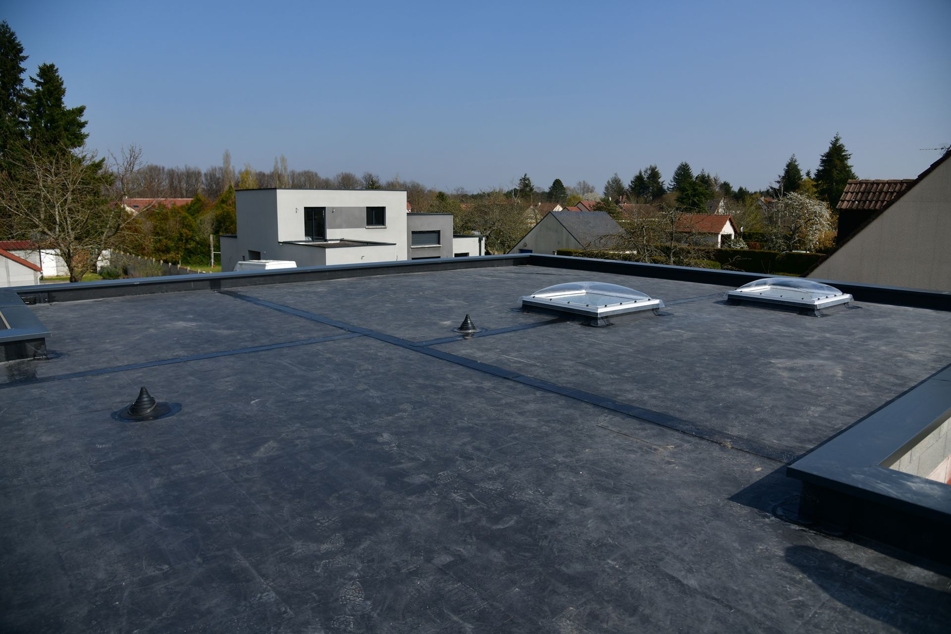 Toiture avec membrane gris foncé, puits de lumière et aérations sous un ciel bleu clair