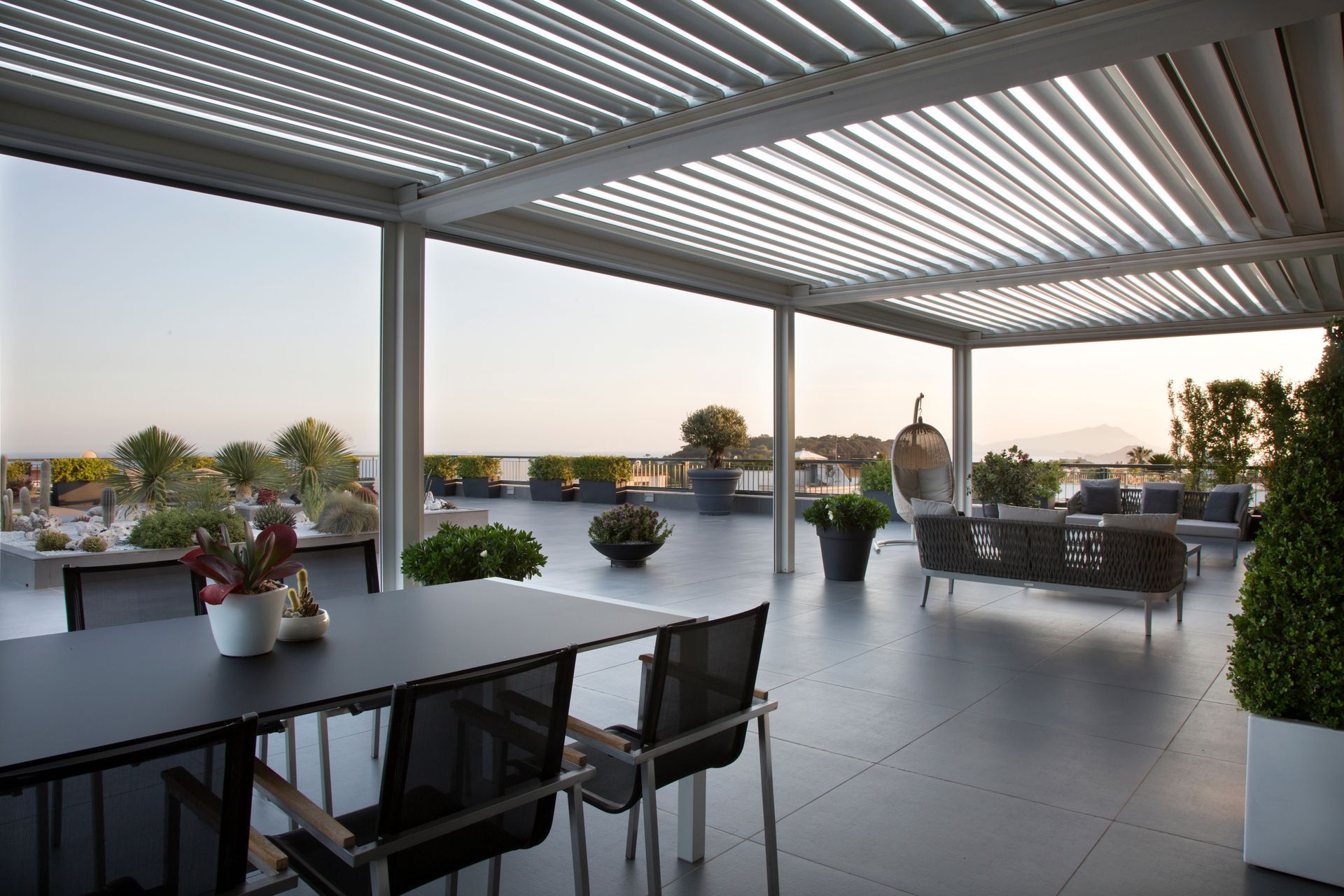 Terrasse sur le toit avec tables, plantes en pot et vue sur la ville au coucher du soleil sous une pergola à claire-voie