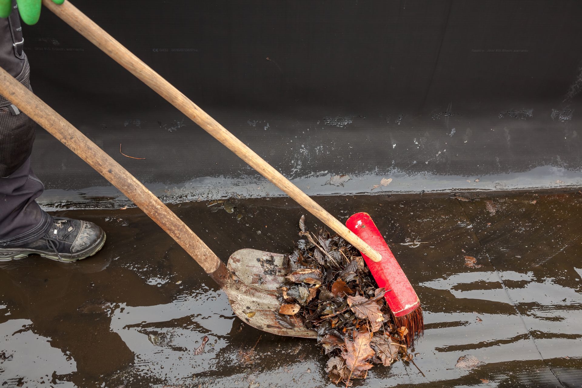 Une pelle rouillée gratte la boue et les débris d'une rue inondée, une botte est visible à côté.