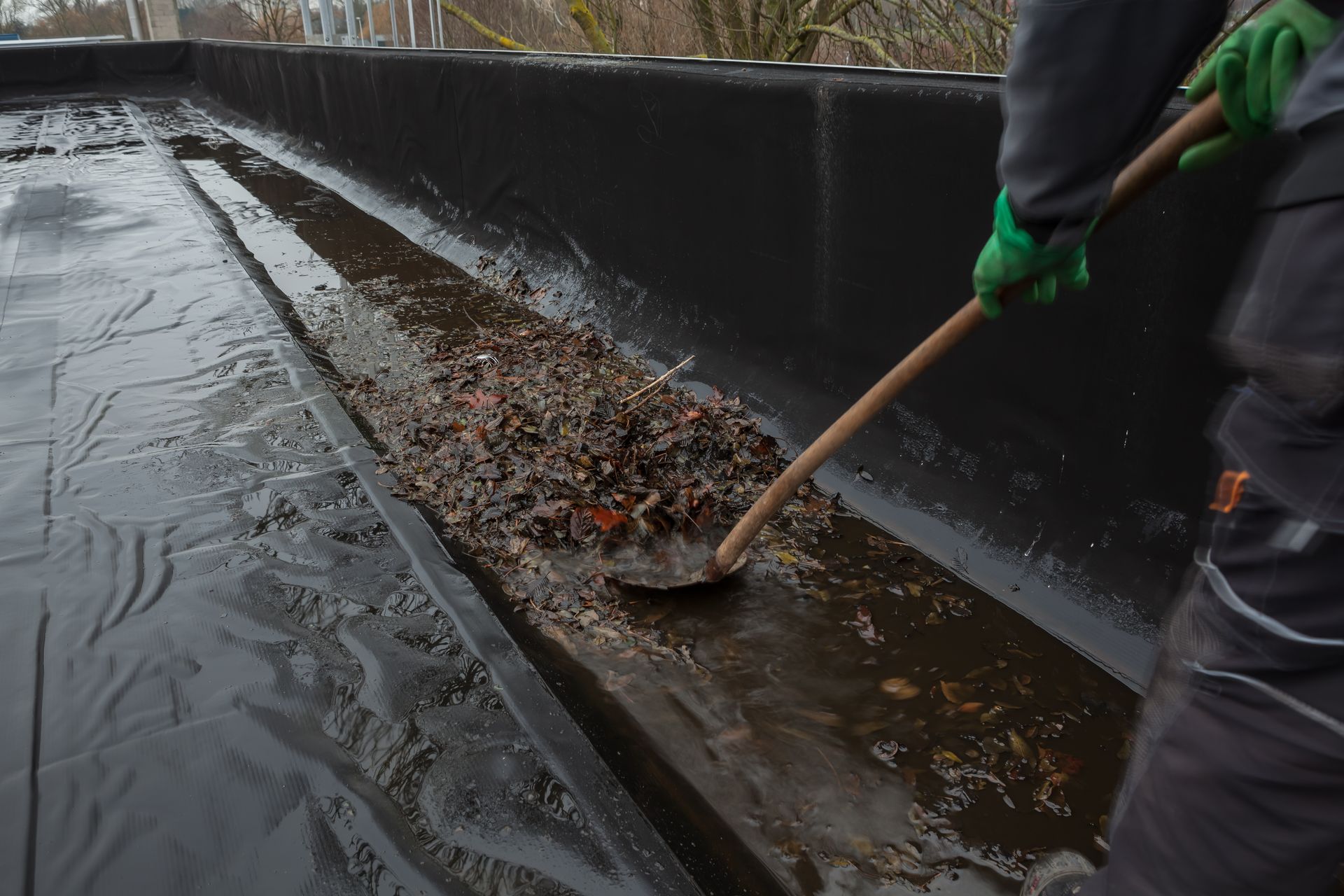 Une personne ratisse les feuilles et les débris d'une gouttière de toit mouillée