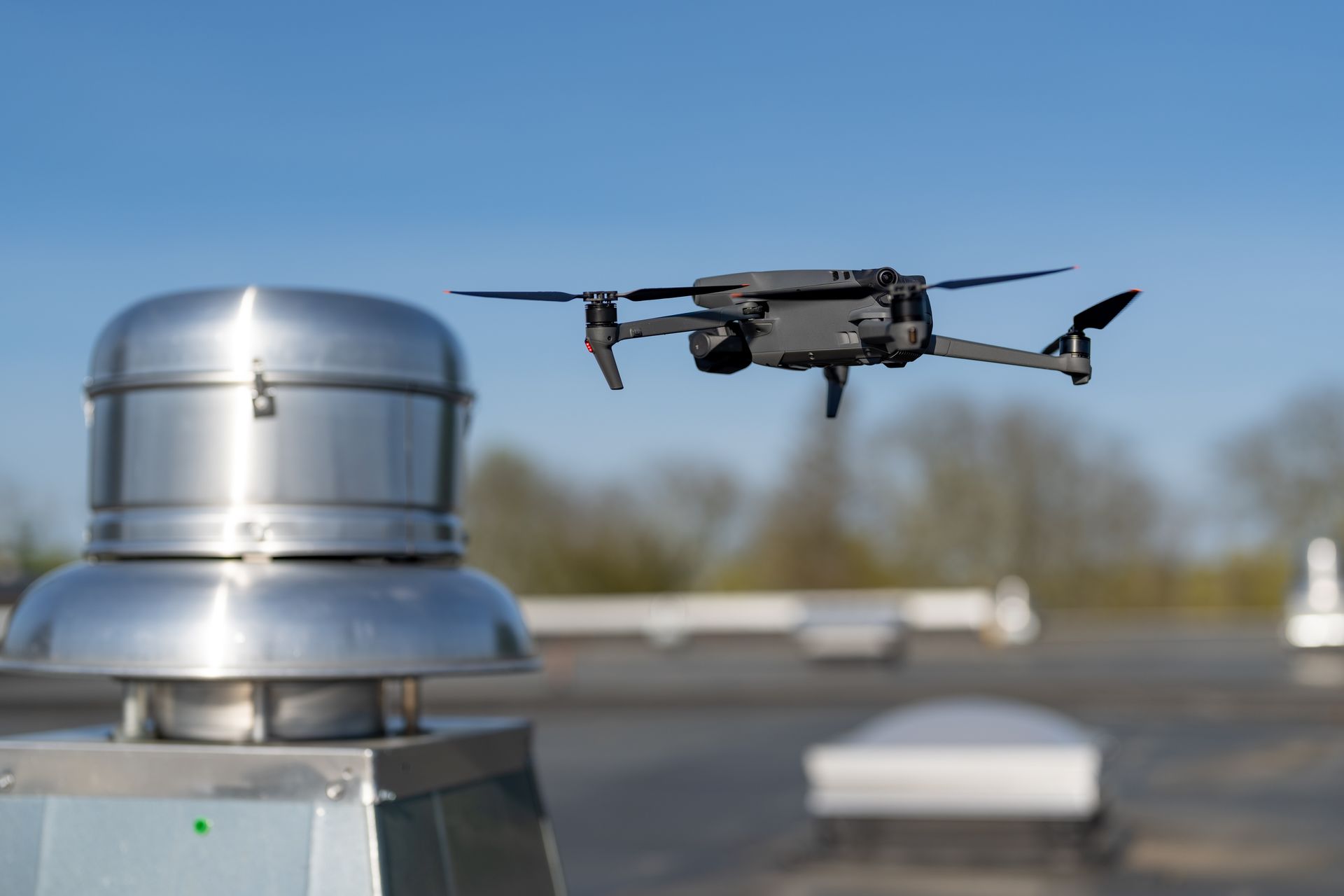 Drone survolant une bouche d'aération sur un toit, se détachant sur un ciel bleu dégagé.