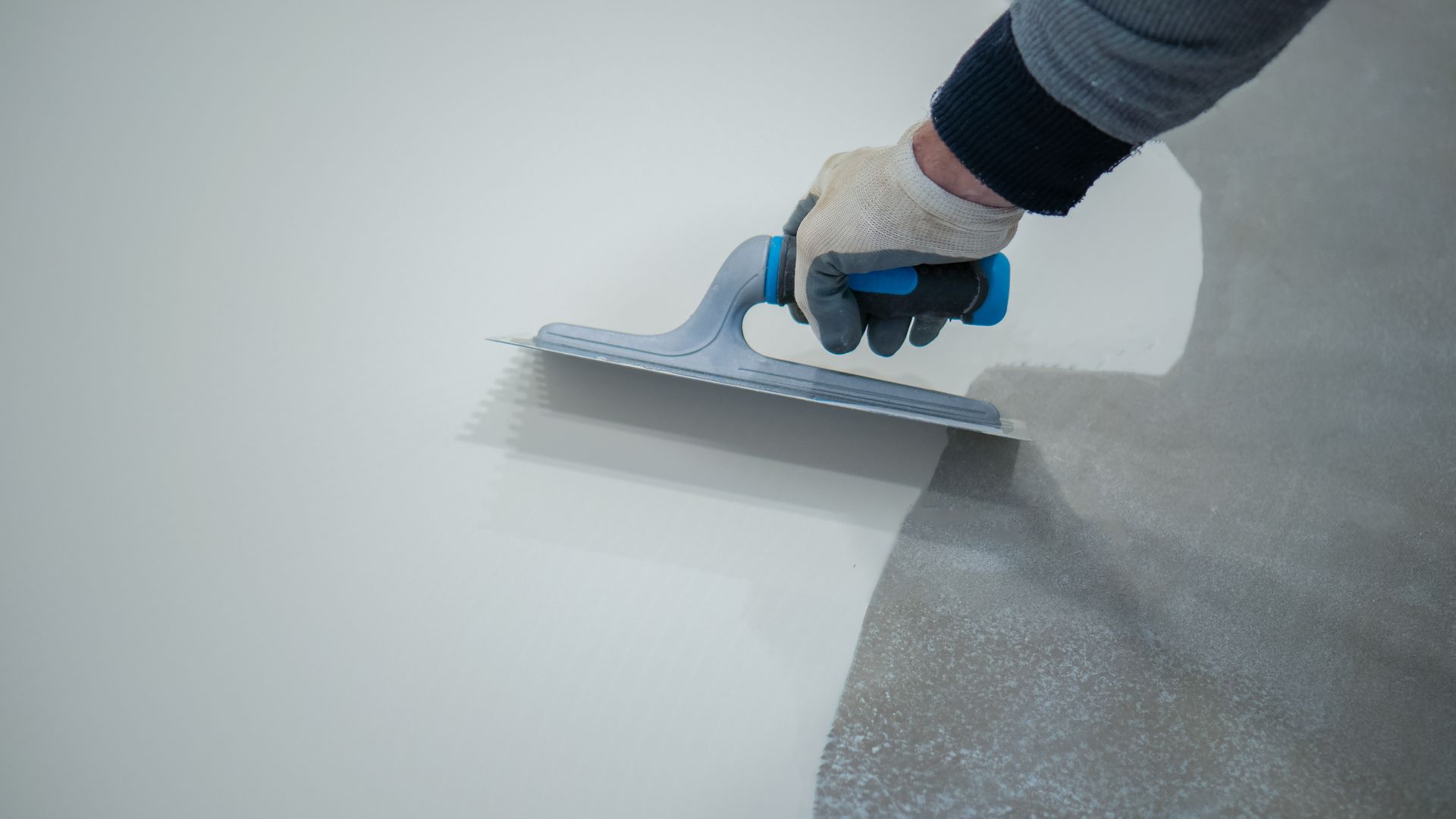 Main gantée utilisant une truelle pour lisser du béton gris humide sur une surface de sol