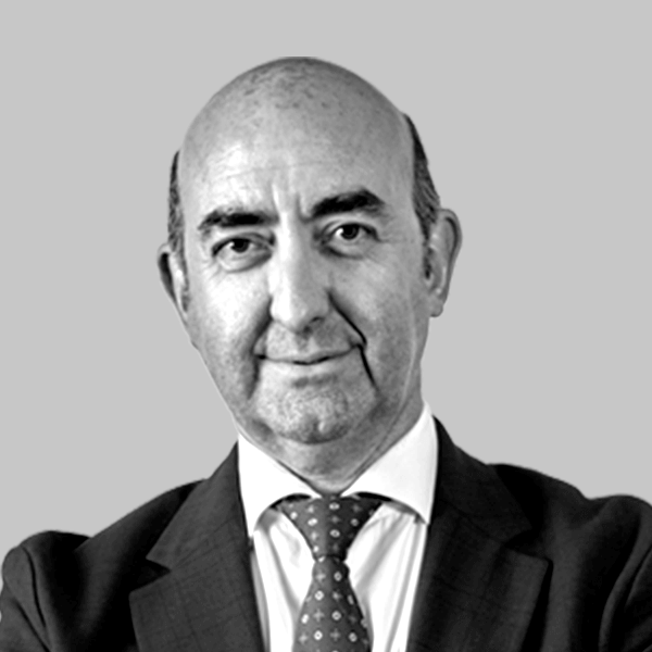 Retrato de estudio de un hombre calvo con traje y corbata estampada sobre un fondo liso.