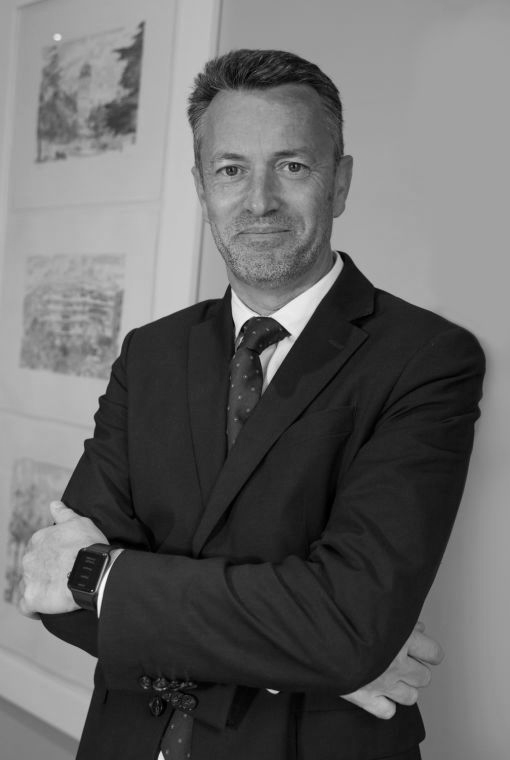 Un profesional con traje y corbata, con los brazos cruzados, de pie en el interior de una vivienda, apoyado contra una pared