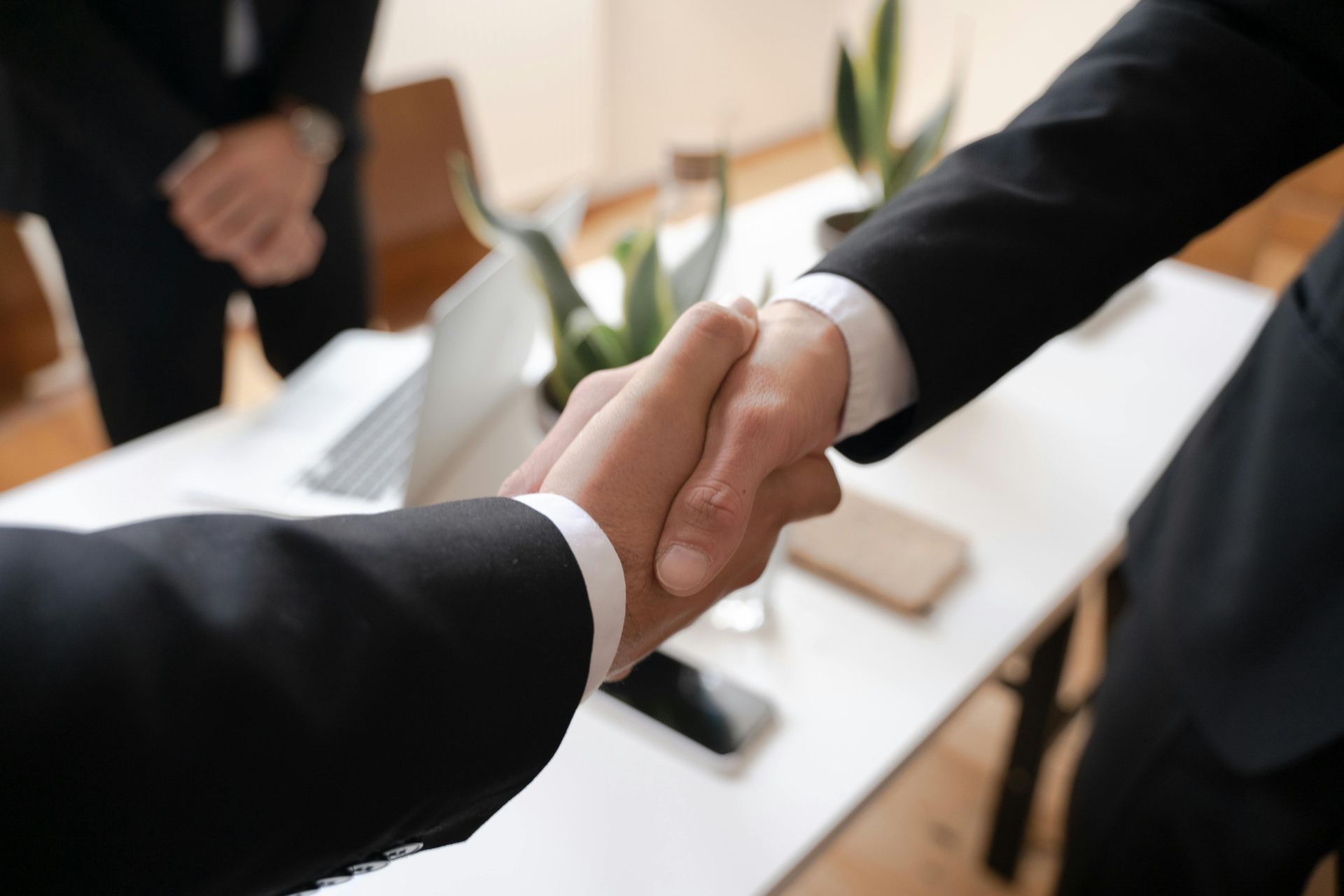 Dos profesionales de negocios vestidos de traje se dan la mano en una oficina con un escritorio y una computadora