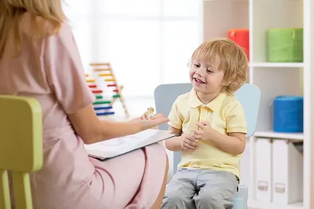 Un niño pequeño está sentado en una silla hablando con una mujer.