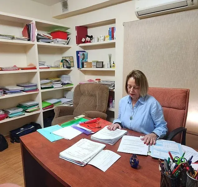 Una mujer se sienta en un escritorio con muchos papeles encima.