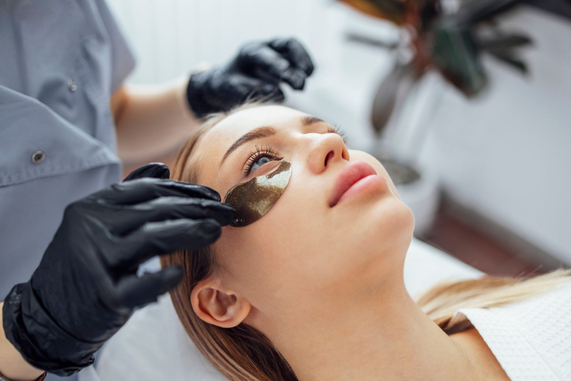 Una mujer está recibiendo un tratamiento facial con parches en los ojos.