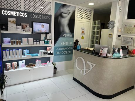 Recepción de una clínica de cosméticos con estantes para productos, carteles y un mostrador frontal curvo.