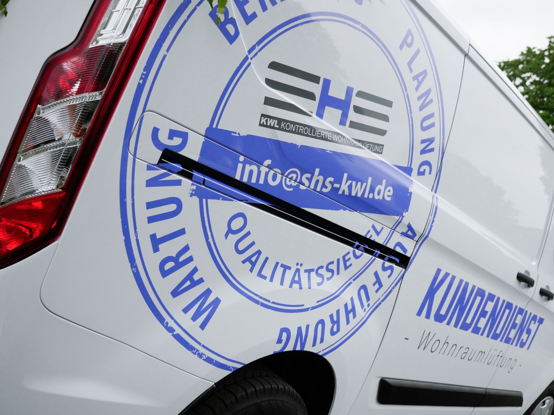 Weißer Lieferwagen mit blauem Logo, auf dem „SHS“ und „Kundendienst“ stehen, sowie Kontaktinformationen und umgebendem Text.