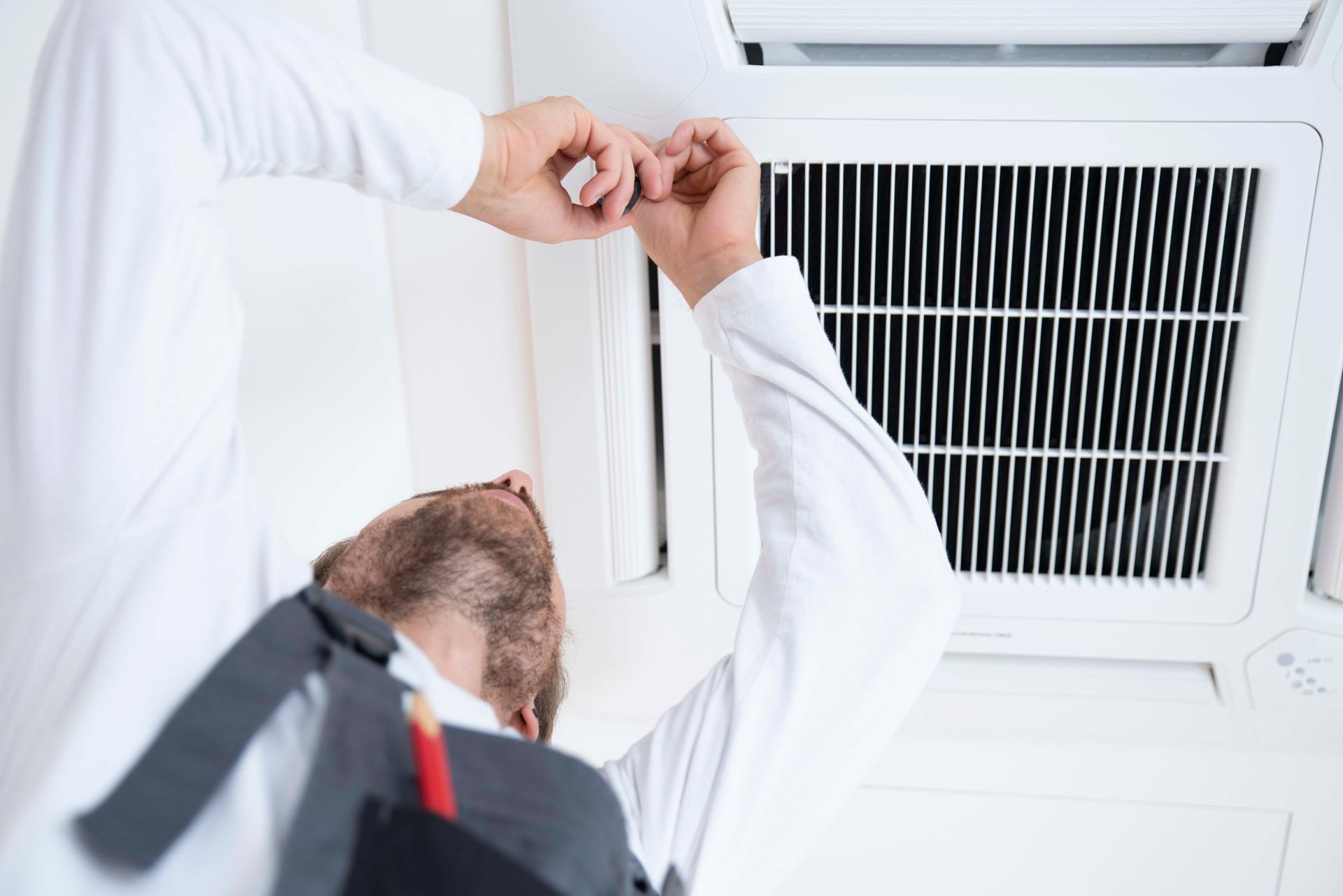 Eine Person in weißem Hemd repariert eine Klimaanlage.