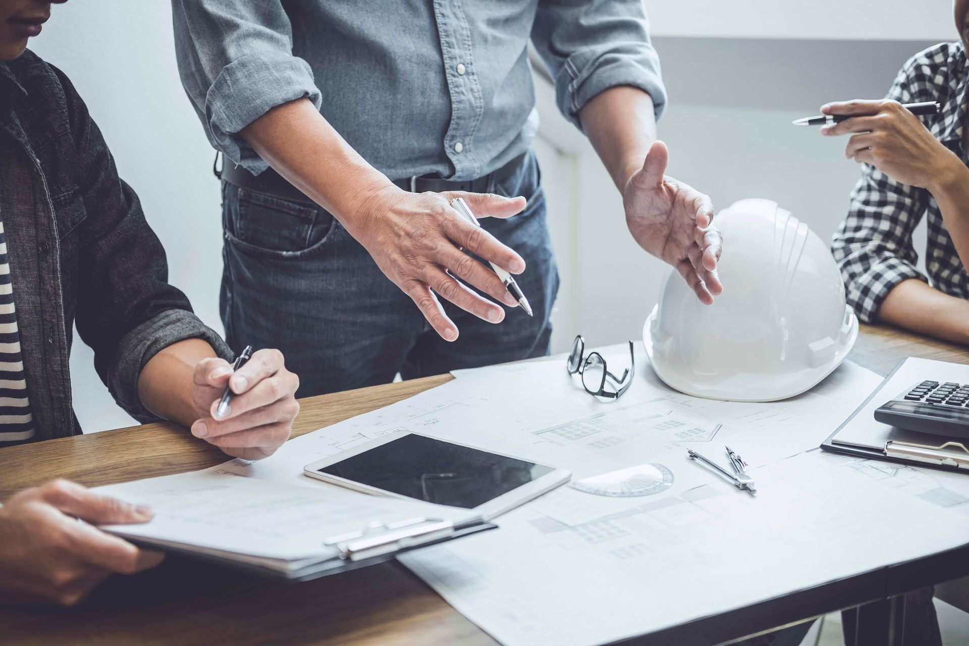 Bauarbeiter prüfen Baupläne; auf dem Tisch liegen ein Schutzhelm und ein Tablet.