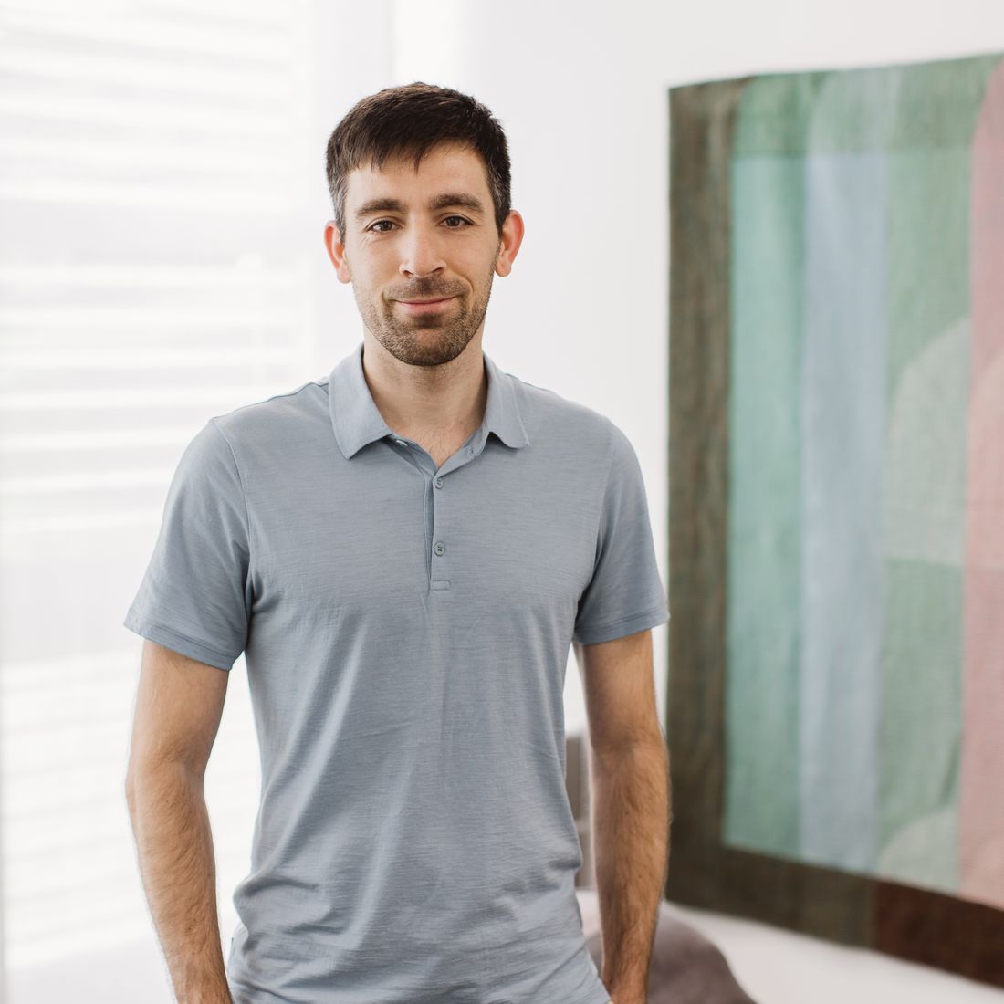 Mann mit dunklem Haar und kurzem Bart, der ein hellblaues Poloshirt trägt.