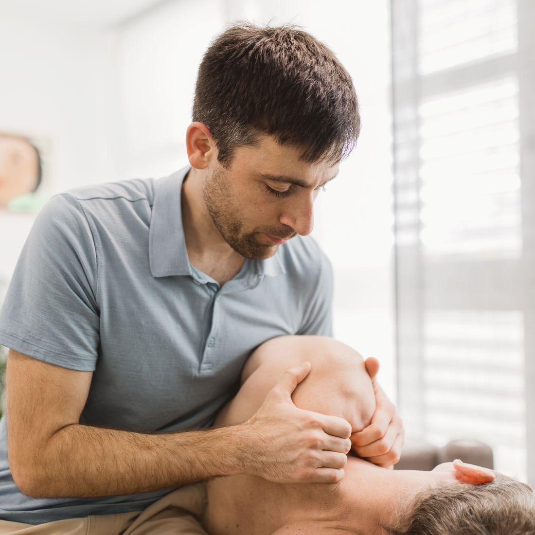 Ein Mann gibt einem anderen Mann in einem hellen Raum eine Nackentherapie. 