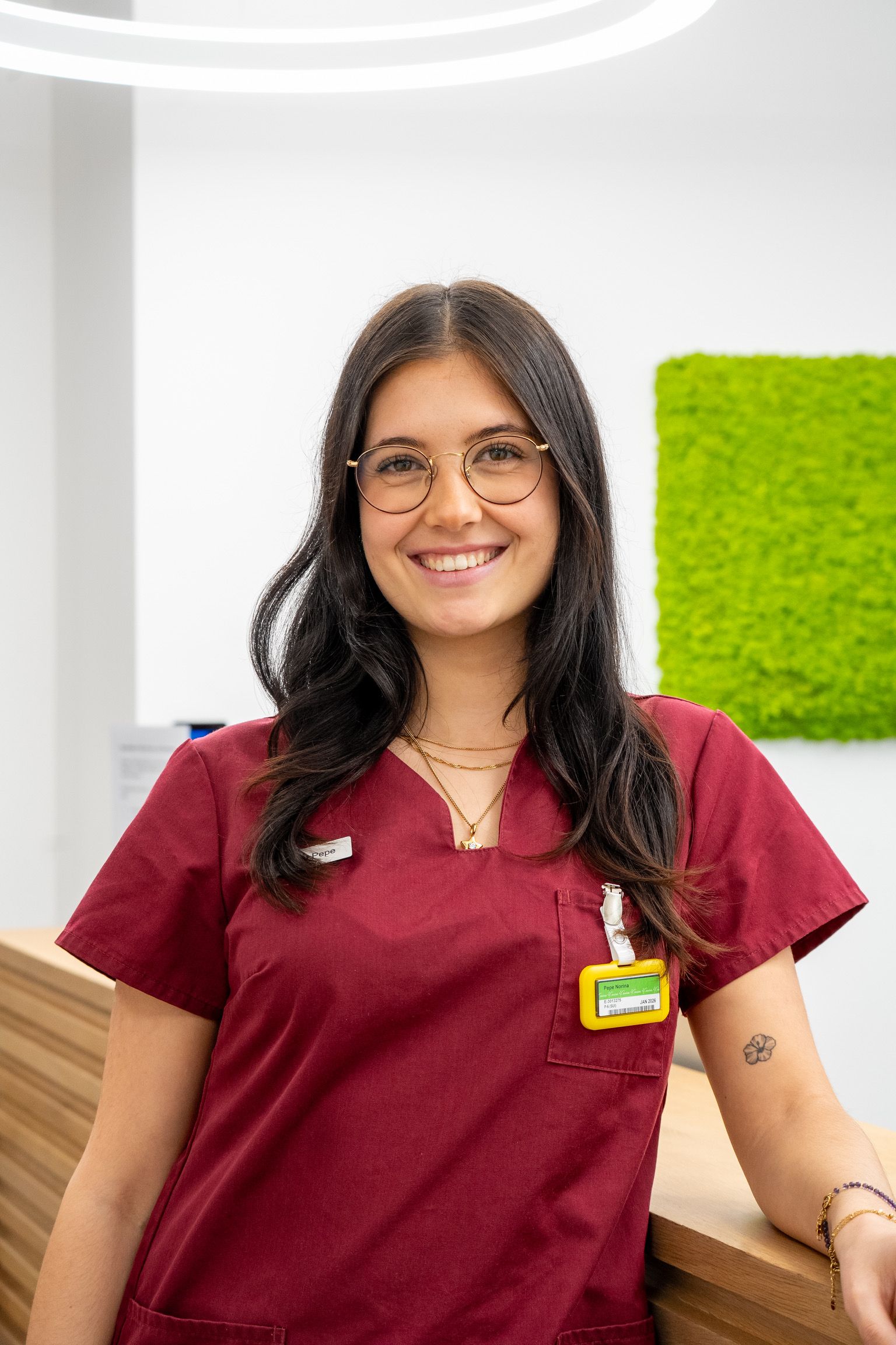 einem Holztresen in einer Arztpraxis. Auf ihrem Arm ist ein kleines Tattoo zu sehen.