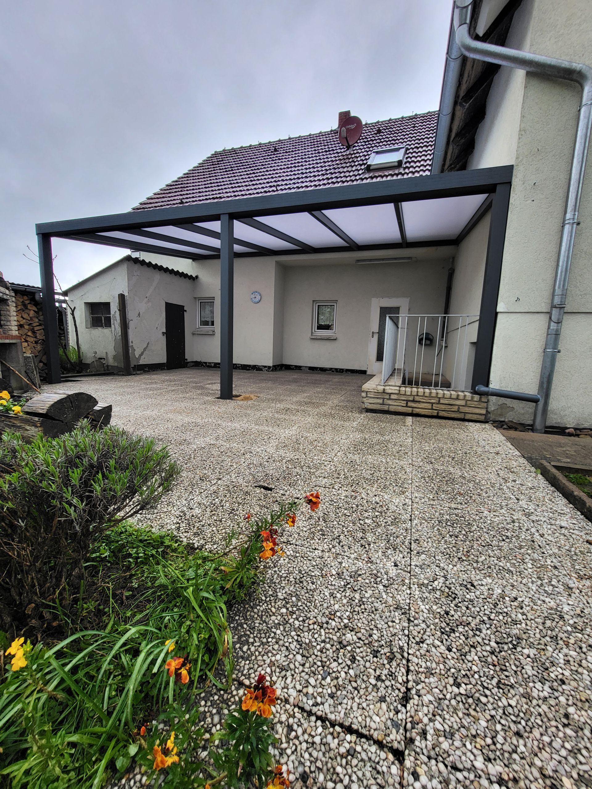Terrasse mit grauen Kiesplatten, Pergola und Haus.