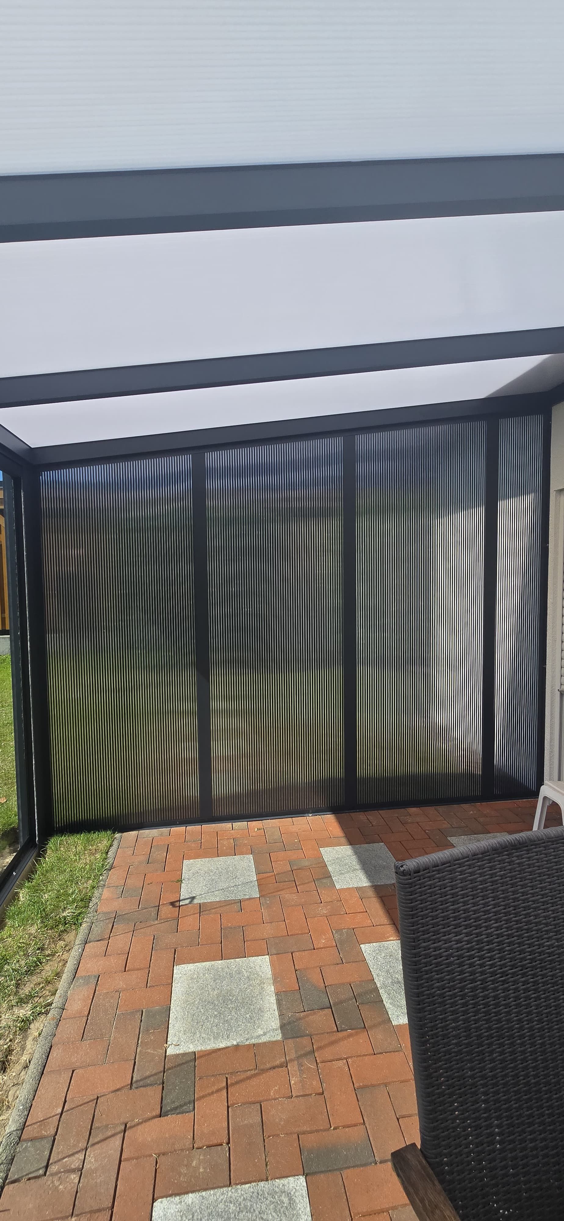 Eine Terrasse mit einem gemauerten Gehweg, der zu einem Gebäude mit einer gestreiften Paneelwand führt.