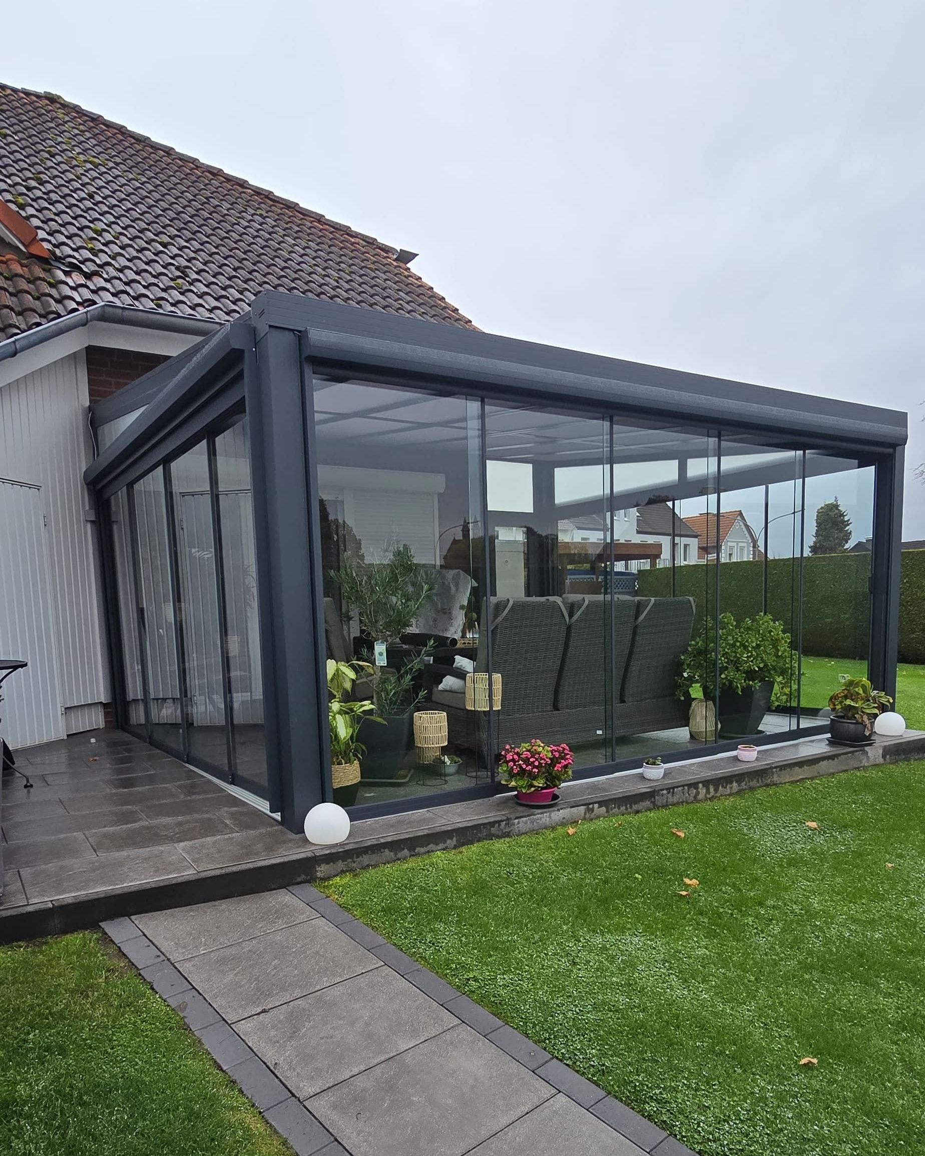 Verglaster Wintergarten mit dunkelgrauem Rahmen, angrenzend an ein Haus