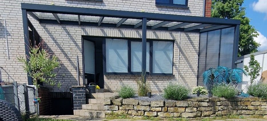 Außenansicht eines Gebäudes mit überdachter Terrasse, Steinmauer und Landschaftsgestaltung.