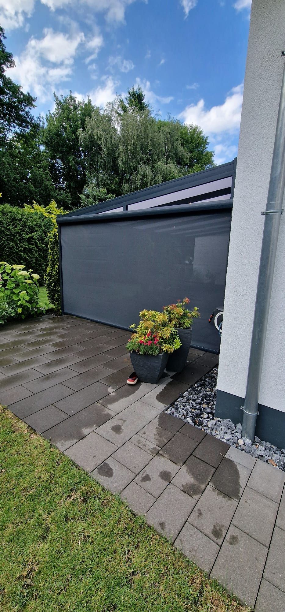 Textiler Sonnenschutz vor einer überdachten Terrasse mit Blumentöpfen auf einer Terrasse