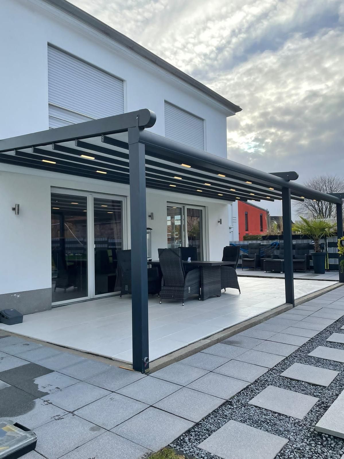 Pergola überdeckt die Terrasse mit Gartenmöbeln, an einem weißen Haus befestigt