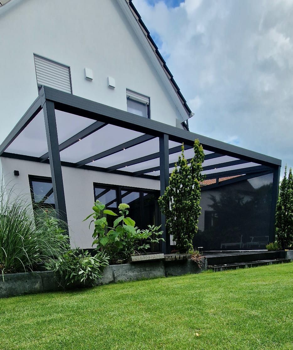 Hinterhofterrasse mit dunkler Pergola über dem Sitzbereich, angeschlossen an ein weißes Haus