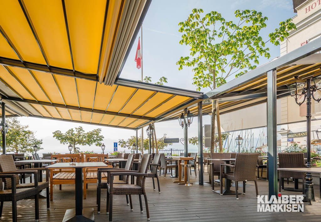 Ein Restaurant mit Tischen und Stühlen unter einem gelben Vordach.
