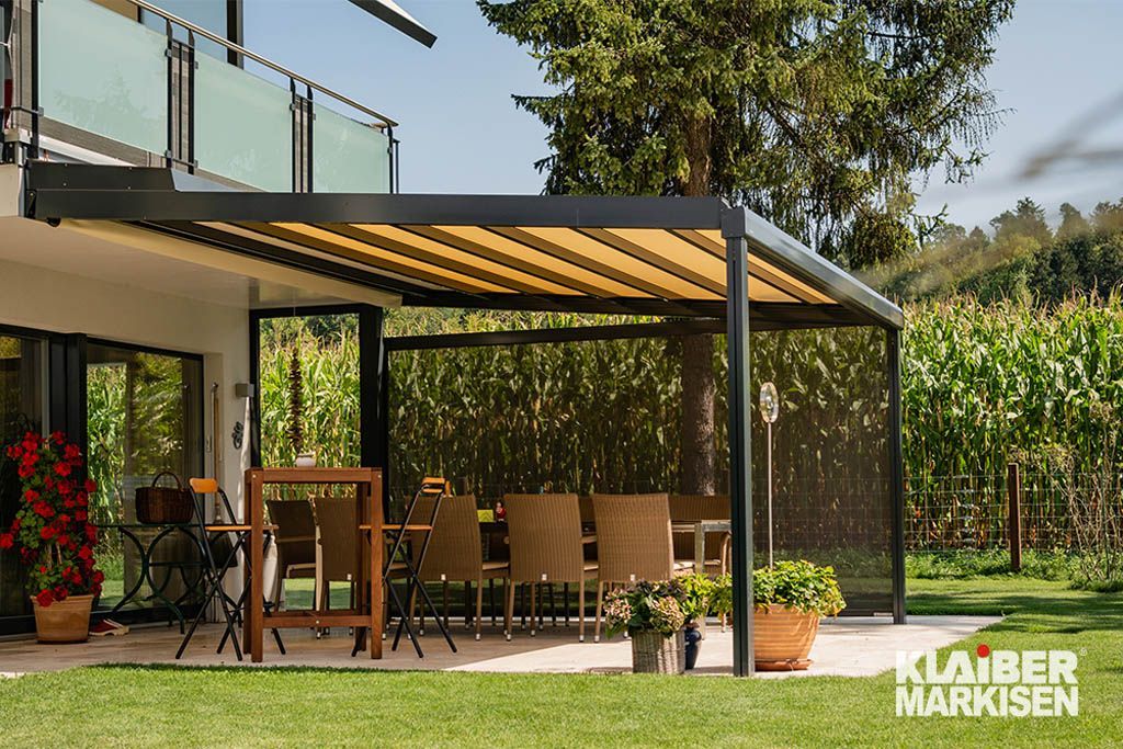 Eine Terrasse mit Pergola und Tisch und Stühlen vor einem Haus.