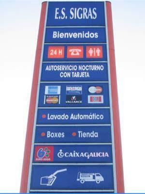 Alto letrero azul y rojo de gasolinera con texto en español sobre servicios, lavado de autos, taquillas y tienda.