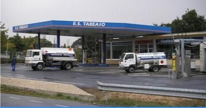 Gasolinera con dos camionetas blancas de servicio estacionadas bajo una marquesina azul mientras llueve.