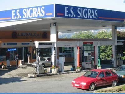 Explanada de una gasolinera con marquesina azul de E.S. Sigras y un coche rojo aparcado delante