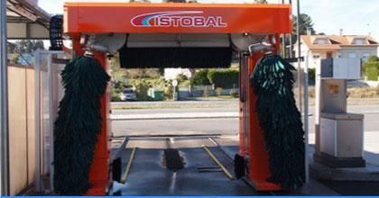 Lavado automático de coches con estructura naranja y cepillos verde oscuro en la entrada de una carretera