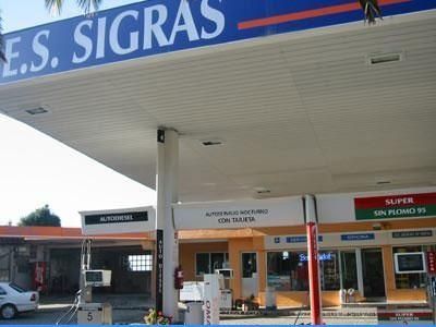 Marquesina de acceso a la escuela con el rótulo «E.S. SIGRAS» y locales comerciales debajo