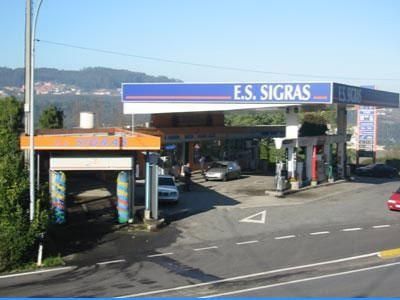 Explanada de una gasolinera con marquesina azul y blanca de E.S. SIGRAS y un túnel de lavado a la izquierda