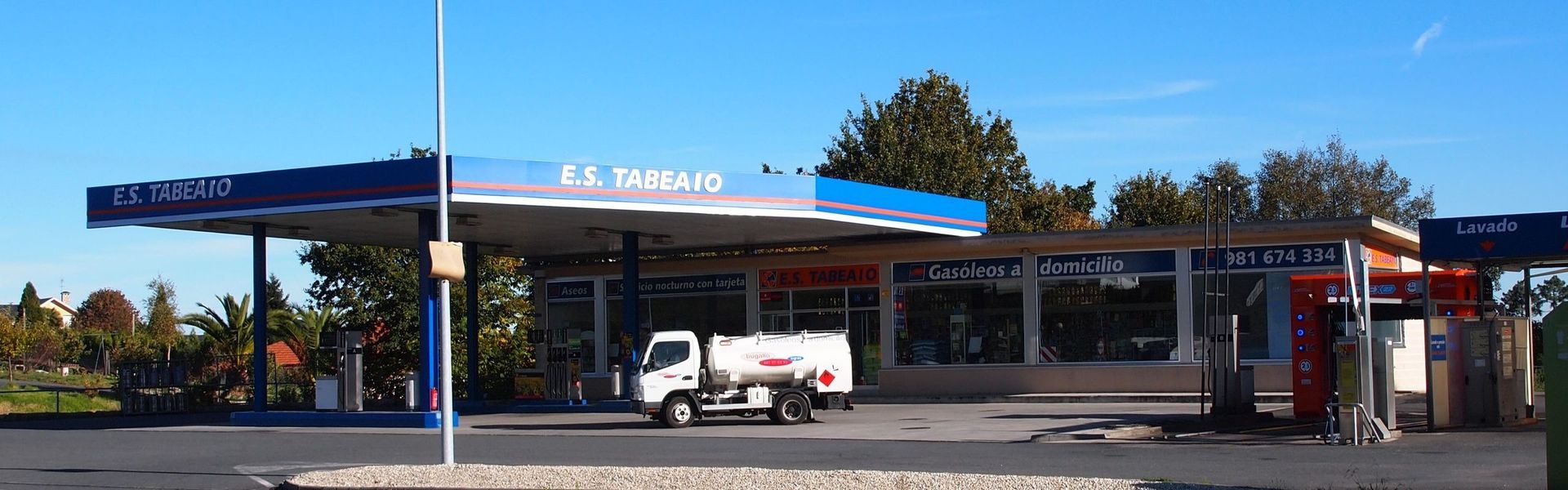 Marquesina de una gasolinera con una camioneta blanca estacionada junto a los surtidores en un día soleado