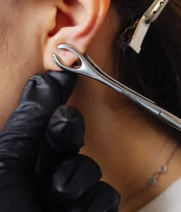 Mano enguantada utilizando una herramienta metálica para perforar orejas para hacer una perforación en el lóbulo de la oreja.