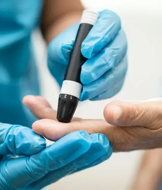 Manos enguantadas utilizando un medidor de glucosa en sangre en la punta del dedo de una persona.