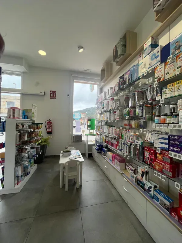 Pasillo estrecho de tienda de conveniencia con estantes de bocadillos y suministros, un taburete blanco y una puerta.