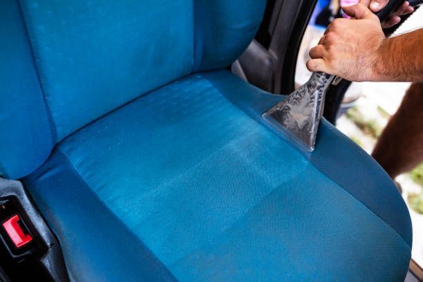 Uma pessoa está limpando um assento de carro azul com um aspirador de pó.