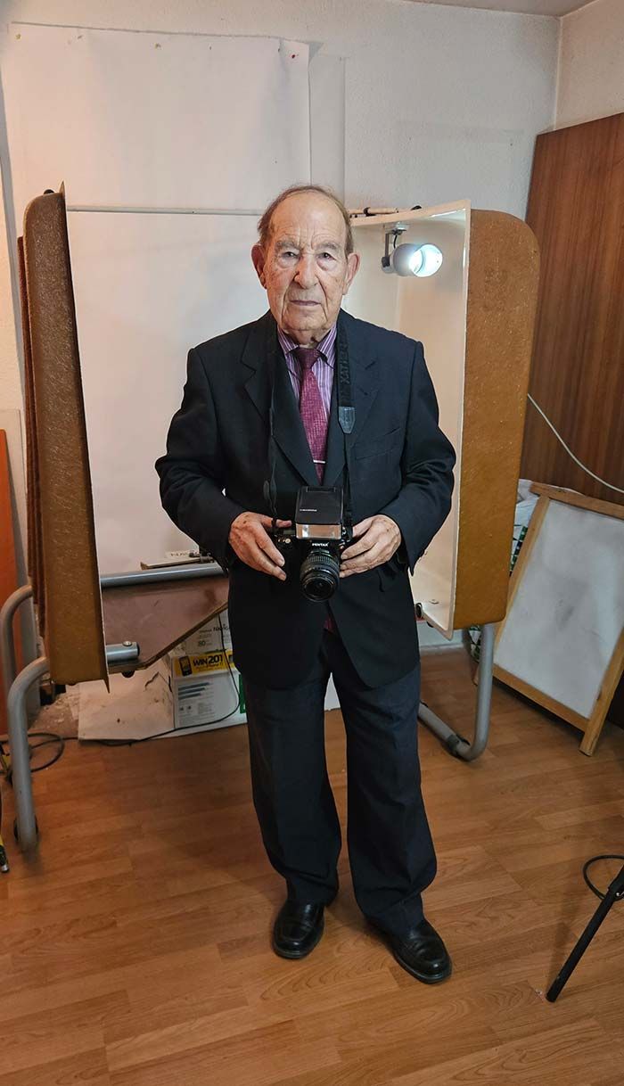 Hombre de traje sosteniendo una cámara en un estudio desordenado.