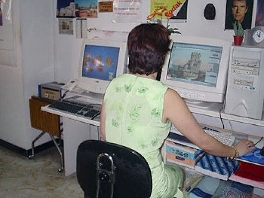 Mujer sentada en un escritorio con dos monitores de computadora; ella está usando uno y el otro muestra una imagen.