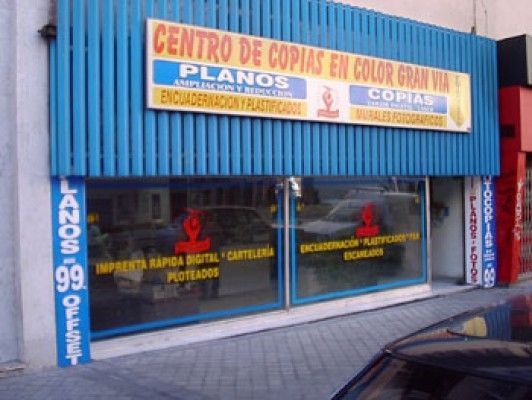 Exterior de un centro de copias con fachada y ventanas de color azul, que ofrece servicios de impresión.