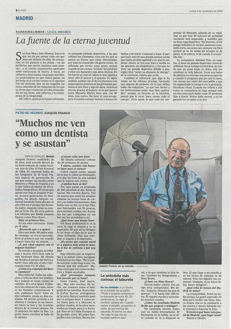 Un anciano sostiene una cámara, frente a un fondo de estudio fotográfico, para un artículo de periódico.