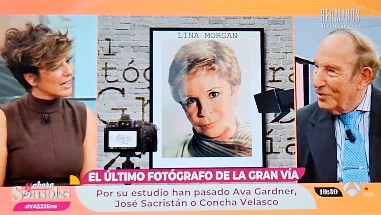 Una mujer entrevista a un hombre junto a una foto enmarcada. El texto dice: «El último fotógrafo de la Gran Vía».