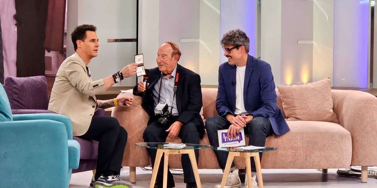 Tres hombres en un programa de entrevistas. Uno sostiene cartas, dos hombres están sentados en un sofá.