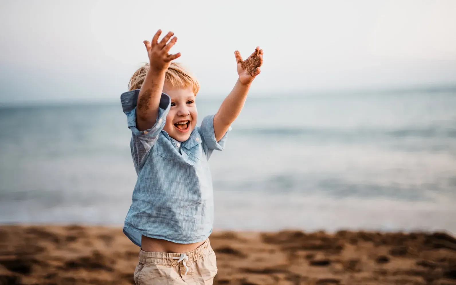 Un niño pequeño está parado en una playa con los brazos en el aire.