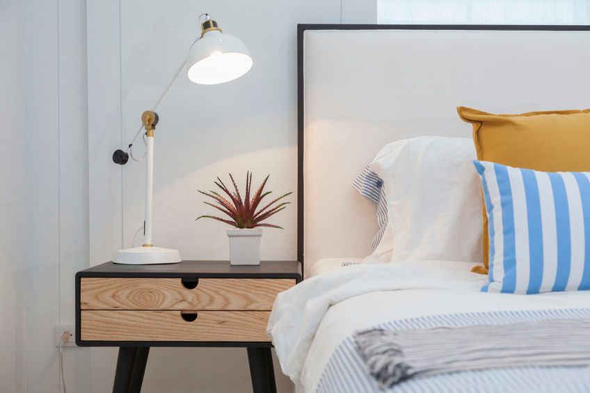 Una mesita de noche con una lámpara y una planta suculenta junto a una cama con almohadas de rayas blancas, amarillas y azules.