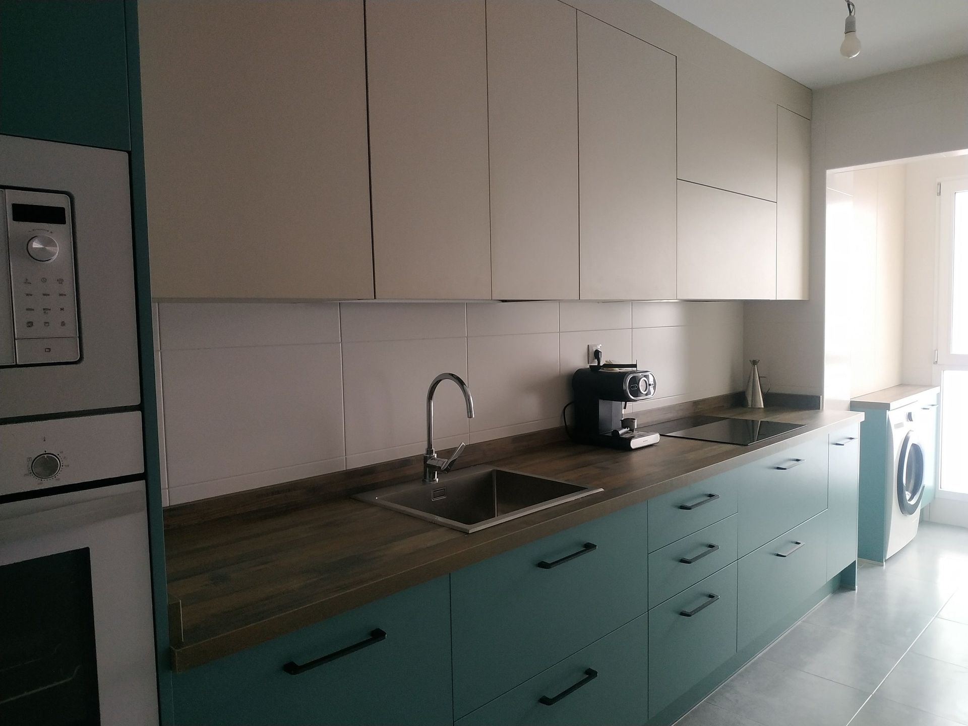 Cocina moderna con armarios inferiores de color verde salvia mate, armarios superiores de color beige claro y encimera de madera oscura.
