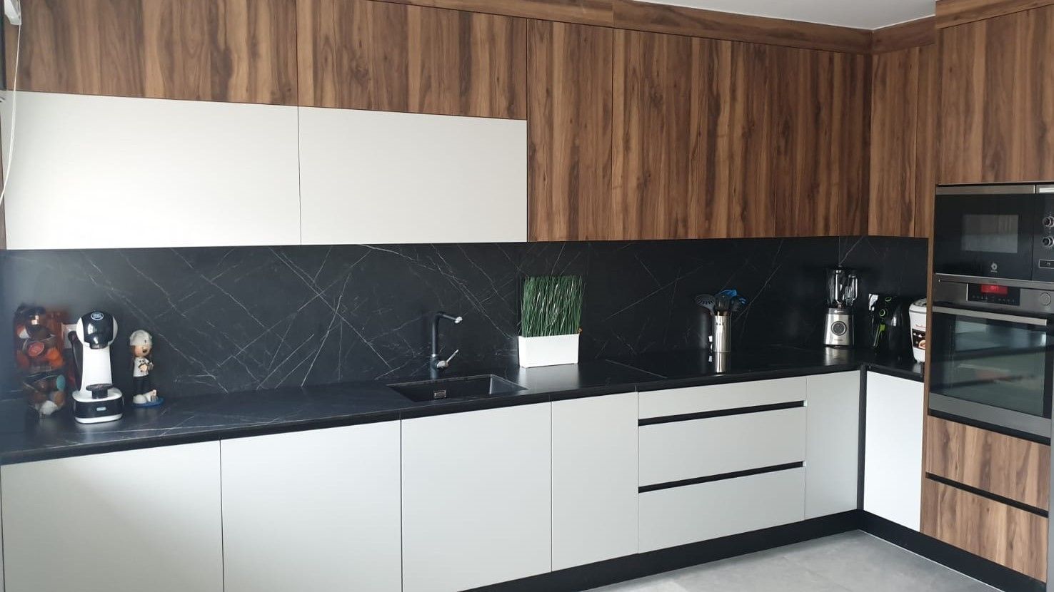 Una cocina moderna con gabinetes blancos, revestimiento de madera y una encimera negra con protector contra salpicaduras y horno empotrado.